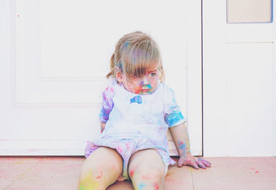 Cute girl looking away with powder paint sitting against door