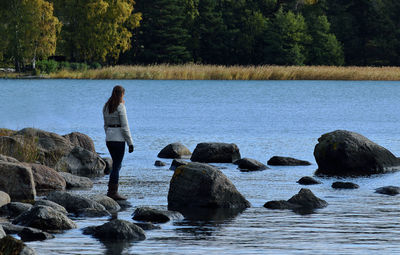 Rear view of woman standing on rock by lake