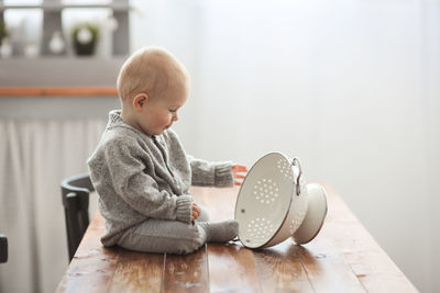 Baby of 10 months plays on the table in the kitchen with kitchen utensils