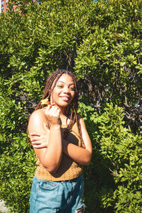 Portrait of smiling young woman standing against plants