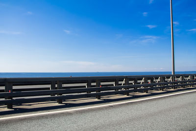 Empty road by sea against blue sky