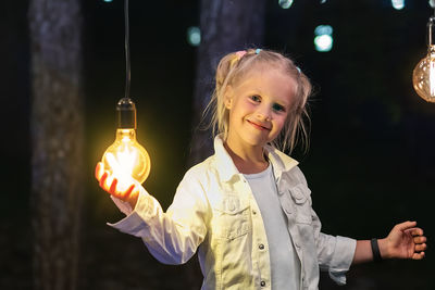Portrait of smiling girl holding illuminated lights at night