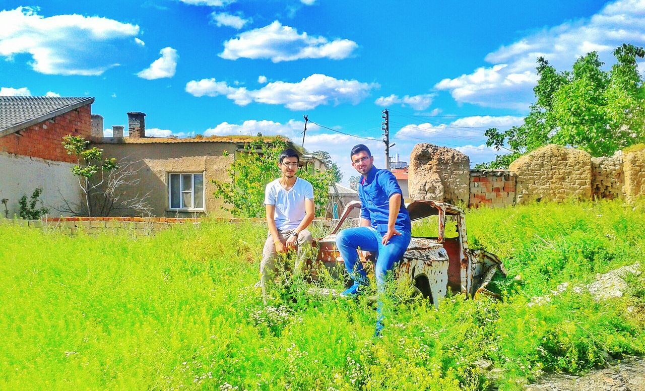 sky, building exterior, grass, architecture, built structure, lifestyles, men, cloud - sky, leisure activity, full length, field, cloud, rear view, blue, casual clothing, person, plant, green color