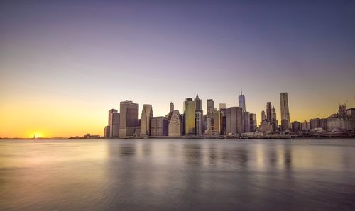 East river by modern buildings against sky during sunset