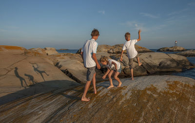 People on rock at beach against sky