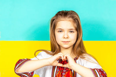 A girl in an embroidered shirt shows a heart sign as a sign of love for ukraine, close-up.