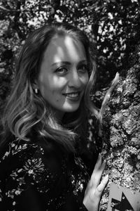 Portrait of smiling young woman standing by rock in park