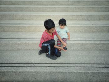 Brother helping sister in wearing shoe on steps