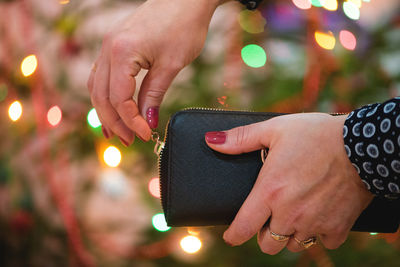 Cropped hands of woman opening purse illuminated christmas tree
