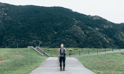 Man wearing mask standing on footpath against mountain