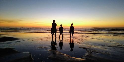 Silhouette people on beach against sky during sunset