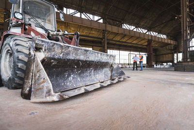 Two men with plan wearing safety vests talking in old industrial hall