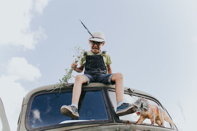 Low angle view of boy sitting against sky