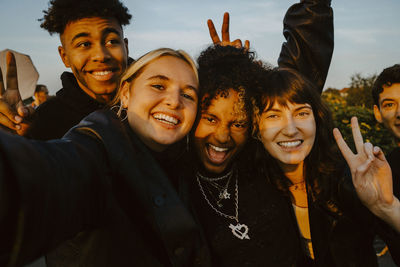 Portrait of cheerful friends taking selfie outdoors during sunset