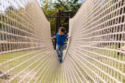 Curly-haired boy crossing a net bridge. development of the agility and courage of the child.