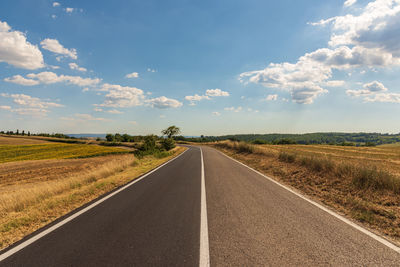 Empty road amidst field against sky