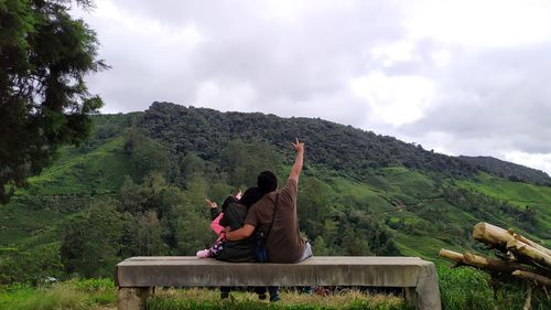 Rear view of men sitting on mountain against sky