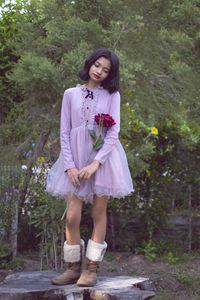 Full length of girl with flower standing against trees