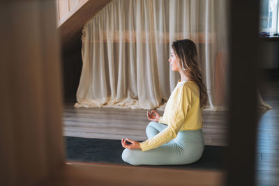 Young slim fitness blonde woman practice morning yoga near window of the home