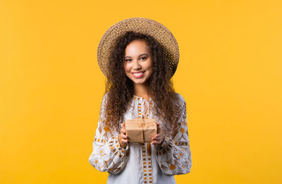 Portrait of young woman standing against yellow background