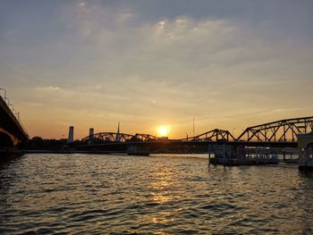 Silhouette bridge over river against sky during sunset