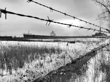 Barbed wire on field against sky during winter