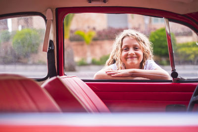 Portrait of smilng blond girl leaning on car window looking inside