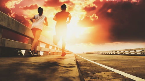 People standing on bridge against sky during sunset