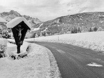 Snow covered road by mountains against sky