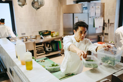 Male chef passing broccolini container while working in commercial kitchen
