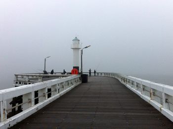 Pier leading towards lighthouse at seaside during foggy weather