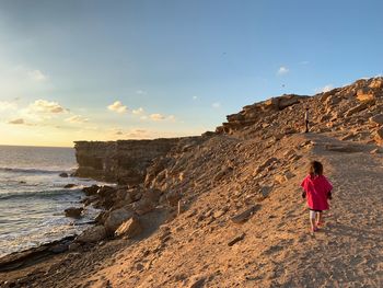 Rear view of girl walking at beach against sky