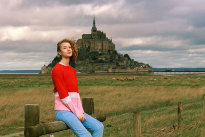 Portrait of young woman on field against the mont-saint-michel