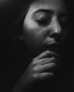 Close-up of young woman with closed eyes and hand on chin in darkroom