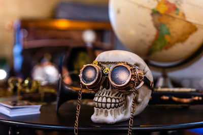 Skeleton head with steampunk glasses on defocused background with globe and old car - image