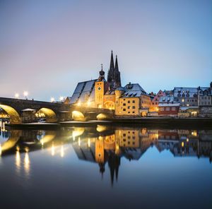 Reflection of illuminated buildings and bridge in river at dusk