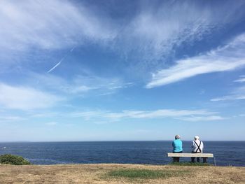 Rear view of senior couple sitting on bench while looking at horizon