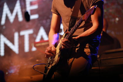 Midsection guitarist performing on stage at music concert