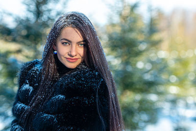 Cheerful young woman in a warm fur coat enjoying a winter day in the snowy forest