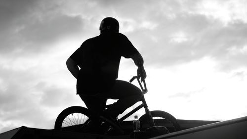 Low angle view of silhouette man riding bicycle against sky