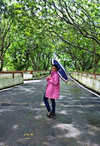 Side view portrait of woman with umbrella standing at park during rainy season