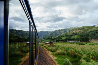 Train by field against green mountains and cloudy sky