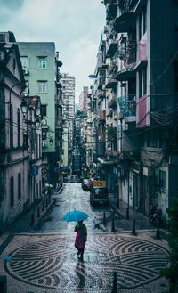 Woman with umbrella walking on street in city during rainy season