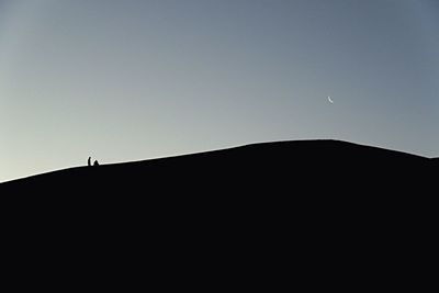 Low angle view of silhouette people on mountain against clear sky