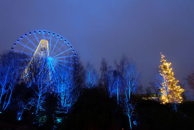 Low angle view of illuminated ferris wheel and bare trees against clear sky at dusk