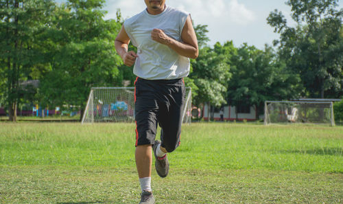 Low section of man running on grassy field at park