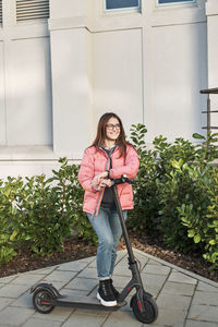 Millennial young girl in a pink jacket on an electric scooter