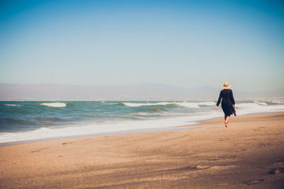 Rear view of woman walking at sea shore against clear sky