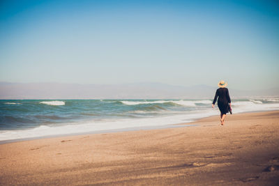 Rear view of woman walking at sea shore against clear sky