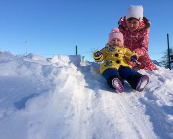 Low angle view of woman with cheerful daughter sliding on snow covered field